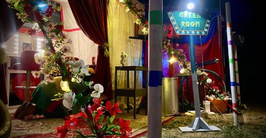 The Green Room sign lit up at night among flowers and velvet curtains
