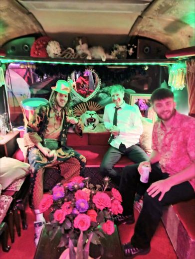 Three friends sitting under green lighting inside The Love Bus with a bunch of roses