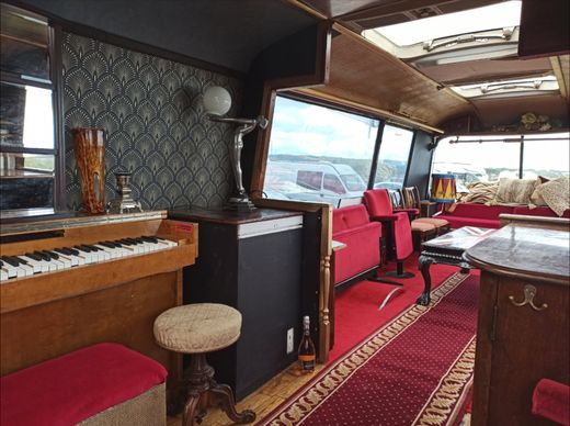The piano, art deco wallpaper and red seating inside The Love Bus in daylight