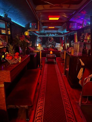 Looking down the red carpeted aisle of The Love Bus at night with fruit, flowers and lamps