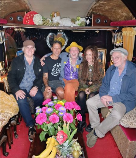 Five friends sitting together inside The Love Bus behind a bowl of pink flowers and fruit