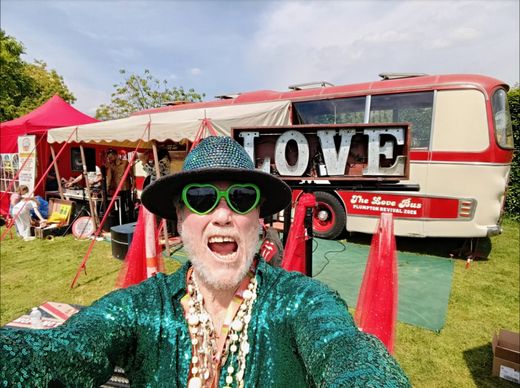 The Great Lorenzo in a green sequin jacket in front of The Love Bus and its LOVE sign at the Plumpton College fete
