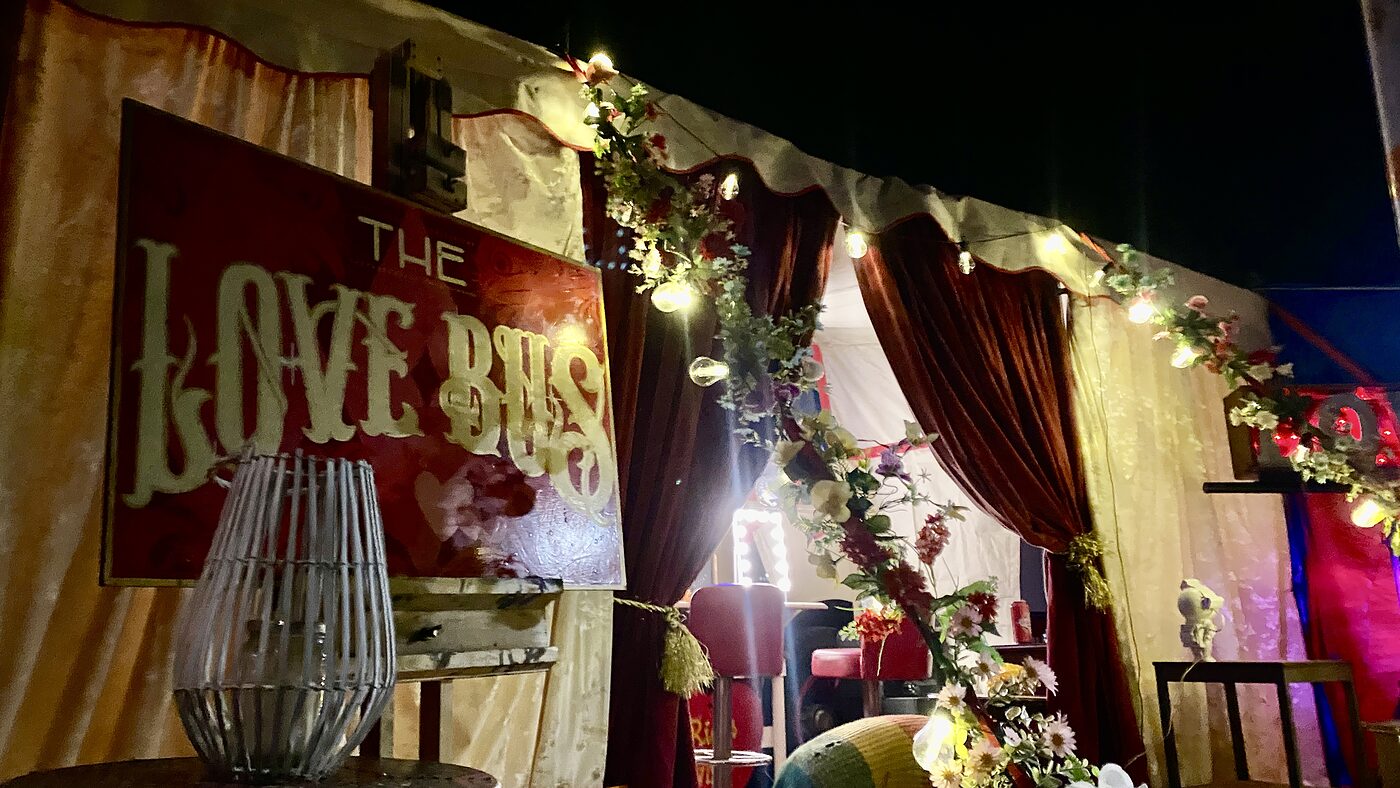 The Love Bus painted sign lit up under the canopy at a festival