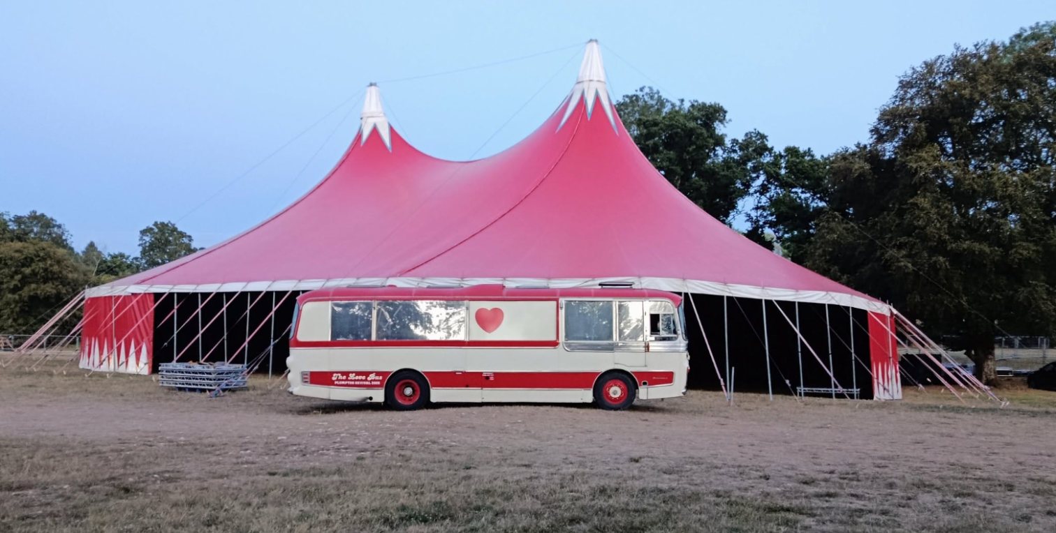 The Love Bus parked in front of the red big top at Mucky Weekender 2026