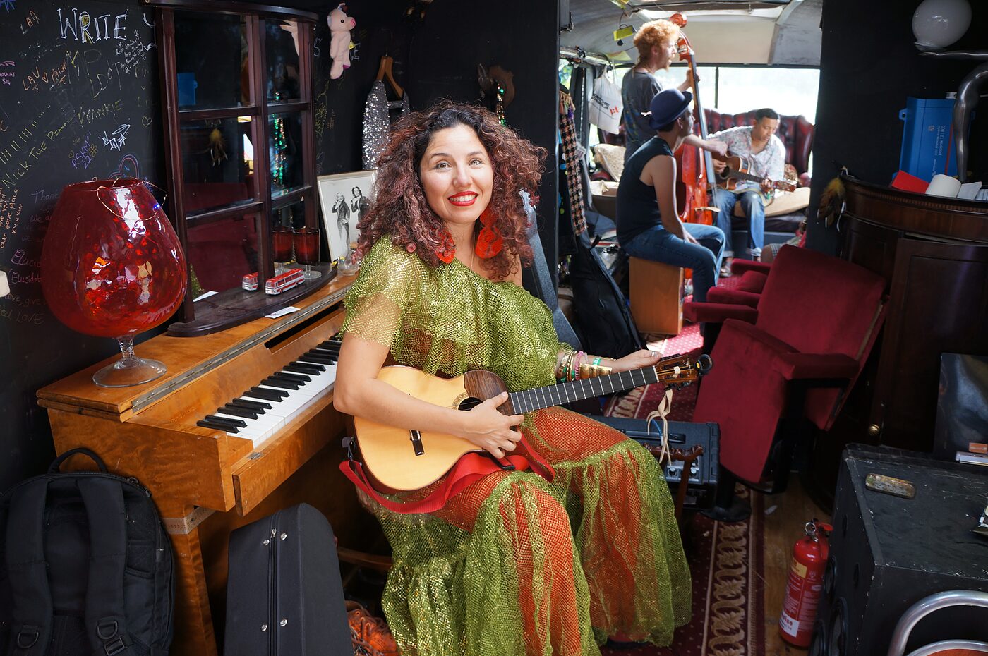 A performer with guitar beside the resident piano on The Love Bus