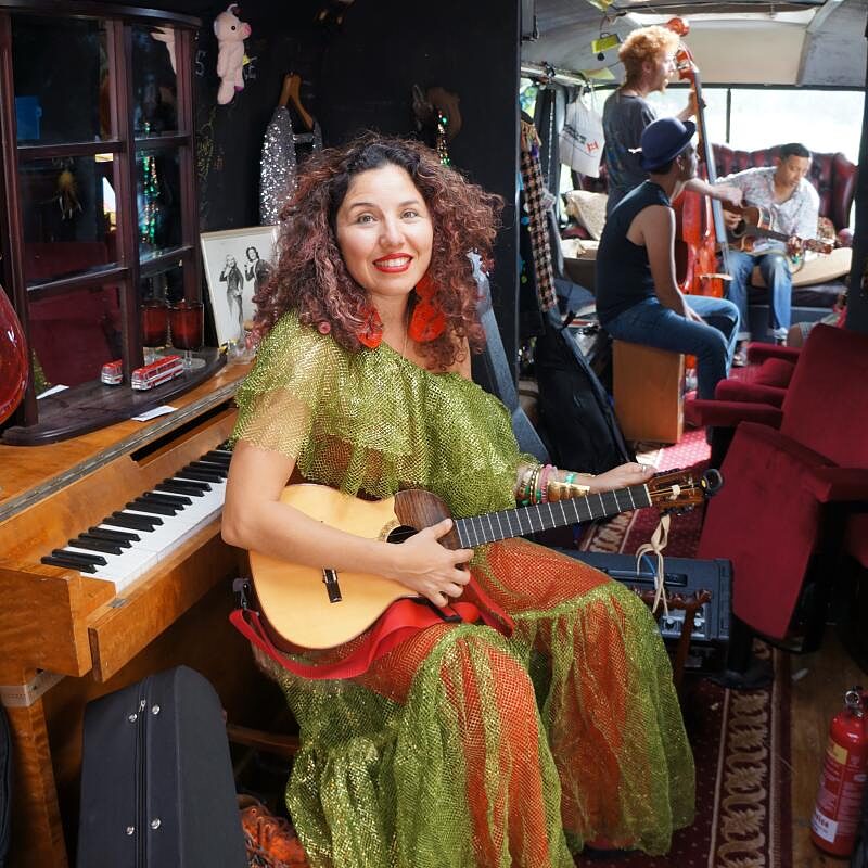 A performer seated with a guitar beside the piano on board